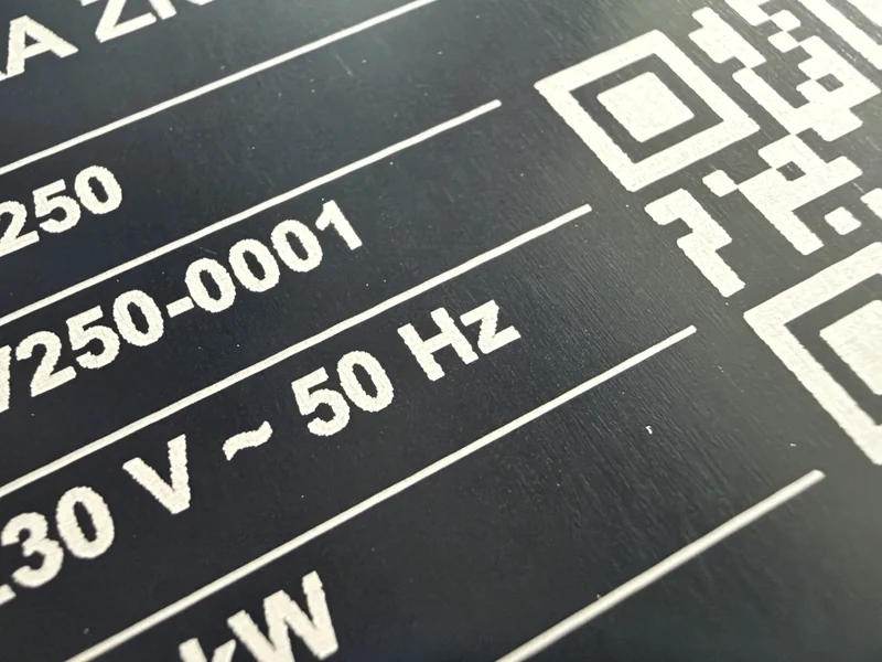 Zbliżenie na wygrawerowany kod QR i numer seryjny na czarnej tabliczce